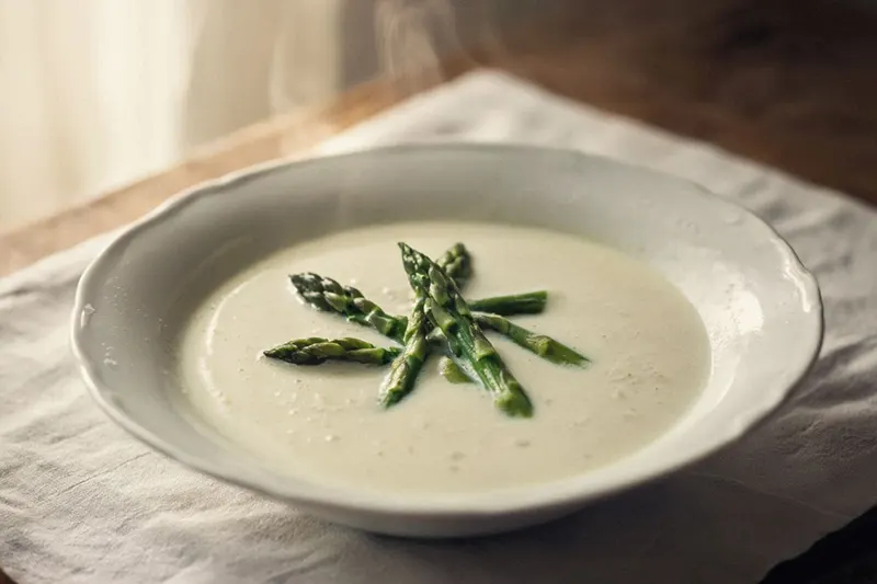A bowl of pale cream asparagus tip soup with tender green asparagus tips arranged on top