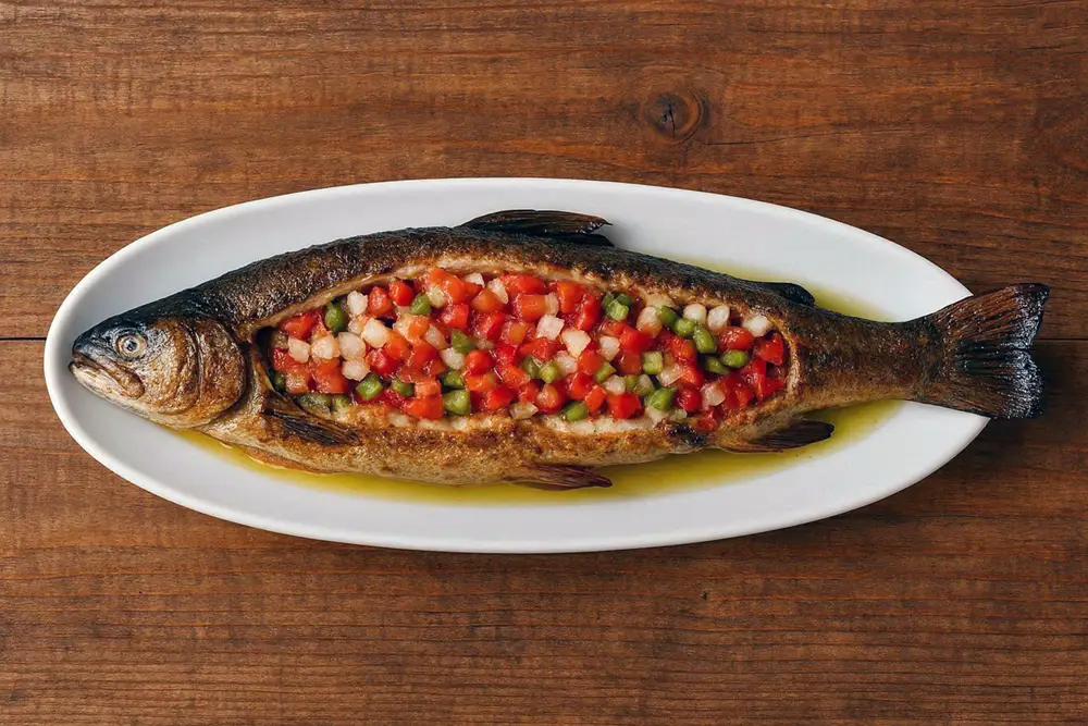 Whole grilled trout on a long ceramic platter, opened along the spine and filled with a colourful raw vegetable stuffing of onion, tomato and green pepper